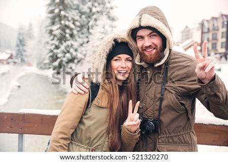 Happy young couple with photo camera standing and showing peace gesture on winter resort
