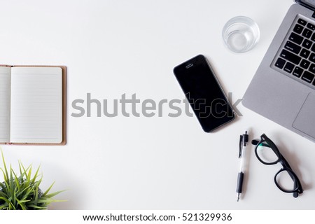 White office desk table with laptop, smartphone, notebook, and glass. Top view with copy space, flat lay.