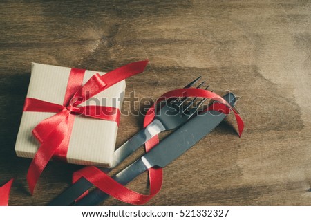 Present and Cutlery Decorated with Red Ribbon on Wooden Background. Selective Focus. Space for Text. Toned image.