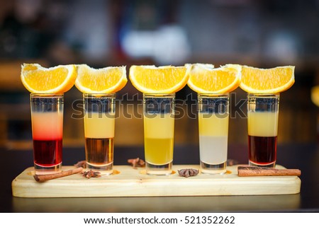 Little alcoholic cocktail at the bar. Multi-colored cocktail. Colorful cocktail at the bar. Orange on the cocktail. Cocktail on the side.