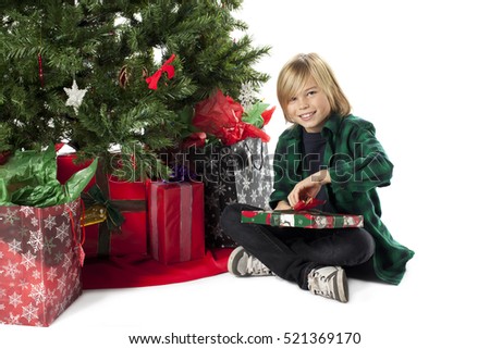 Young boy in santa claus hat opening gifts by a traditional christmas tree with a white isolated background