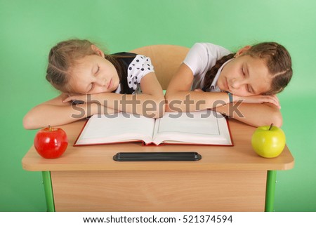 Two school girls sleeping on a stack of books at her desk isolated on green