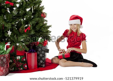 Blonde girl in santa cap opening gifts by the traditional christmas tree
