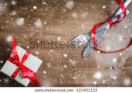 Present and Cutlery Decorated with Red Ribbon on Wooden Background. Selective Focus. Space for Text. Toned image. Snow effect.