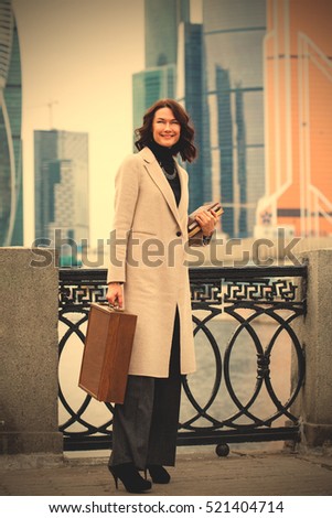fashion. beautiful European woman in a white coat against the backdrop of the city's business district. brunette with a wooden case and books in her hands. instagram image filter retro style