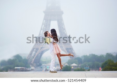 Beautiful romantic couple in love with bunch of white roses having fun near the Eiffel tower on a cloudy and foggy rainy day. Paris, France Royalty-Free Stock Photo #521454409