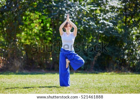 Young woman doing yoga outdoors in tranquil environment. Performing tree pose (vrksasana). Serene relaxed female yoga instructor