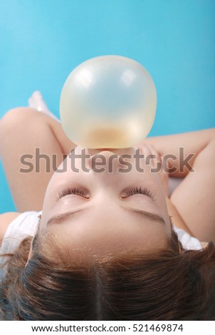 Top view of beautiful young brunette  girl blowing bubble gum isolated on blue