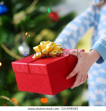 Child in pajamas holding Christmas gift by a Christmas tree on a morning