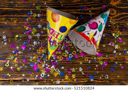 Top view on birthday caps and colorful festive confetti are scattered on a wooden desk