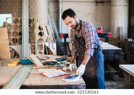 Portrait of a carpenter standing in his woodwork studio and holding digital tablet