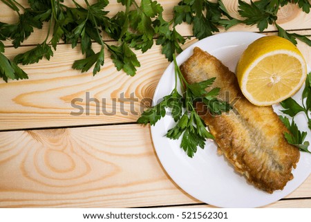 Fried fish with parsley and lemon on a white plate on a rustic background