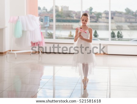 Cute little ballerina in white dress and pointe shoes is dancing in the room. Kid in dance class. Child girl is studying ballet.  Copy space.