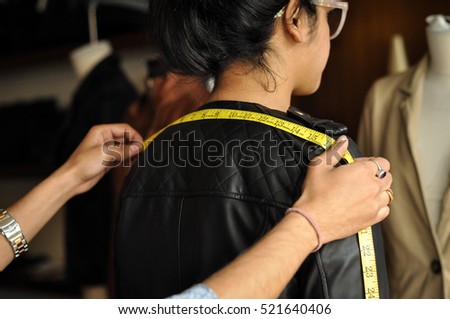 Tailor taking shoulder measurement of a lady customer from back. The face of the customer and the tailor is not visible and identifiable.  Royalty-Free Stock Photo #521640406