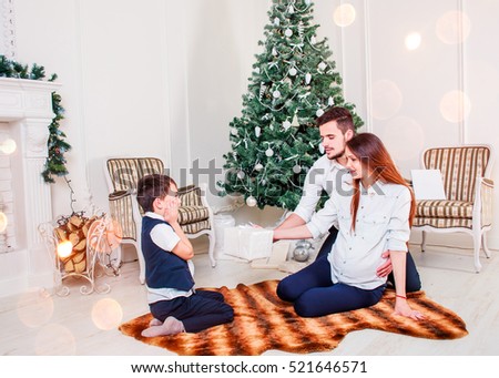 Happy family couple give gifts in the living room, behind the decorated Christmas tree, the light give a cozy atmosphere. New Year and Xmas theme