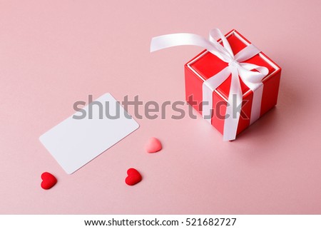 Valentine day composition: red gift box with bow, credit / visiting card template and small hearts on light pink background.