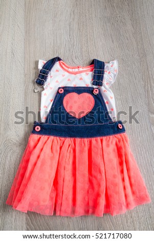 Coral and blue dress, overalls with heart on grey wooden background. Little girl outfit. Top view.