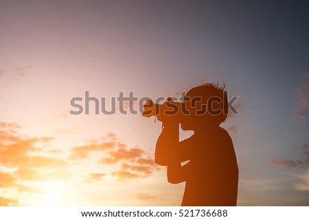 Silhouette of a young man  holding camera, extend the arms while sunset .