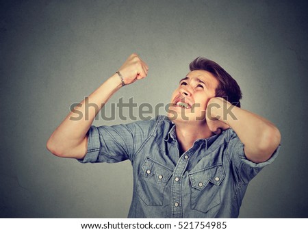 Stressed young man covering his ears having headache looking up isolated on gray background. Negative human emotion face expression