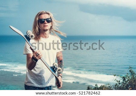 Young man blonde in sunglasses skater in front of amazing sea view 