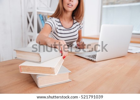 Cropped photo of beautiful female student working with laptop and books in classroom. Focus on woman's hands touching books.