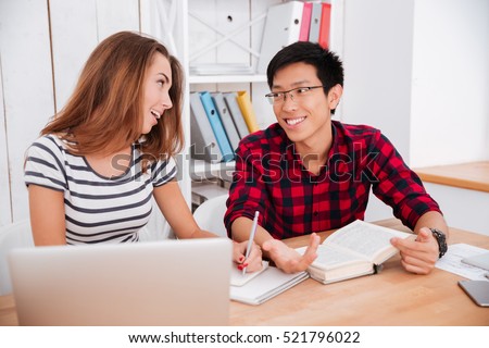 Photo of happy asian boy wearing glasses and girl dressed in t-shirt in a strip print working together for project while sitting at classroom.