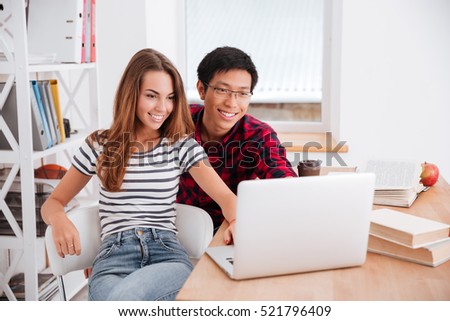 Photo of happy asian boy wearing glasses and girl dressed in t-shirt in a strip print working together for project while sitting at classroom.