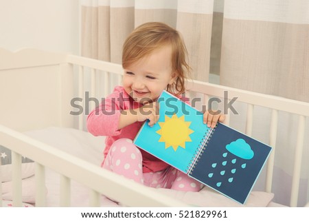 Cute little girl with book in cradle at baby room
