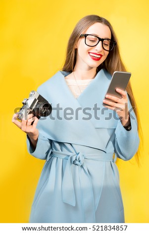 Stylish woman photographer with retro camera and smart phone on the yellow wall background