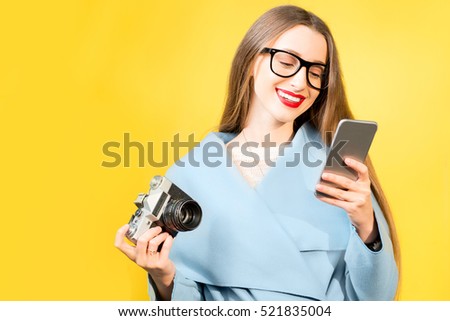 Stylish woman photographer with retro camera and smart phone on the yellow wall background