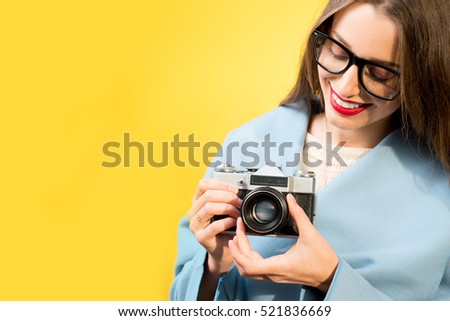 Stylish woman photographer with retro camera on the yellow wall background