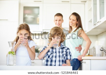 Boy and girl drinking water with lime in the kitchen while the parents are watching Royalty-Free Stock Photo #521846461