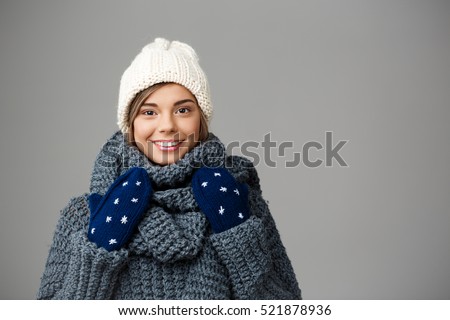 Young beautiful fair-haired girl in knited hat sweater and mittens smiling looking at camera over grey background. 