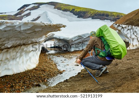 man hiker on the trail in the Islandic mountains. Trek in National Park Landmannalaugar, Iceland. Hiker making photo of glacier near the creek