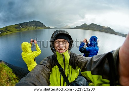 hikers on the Lake coast with mountain reflection at the rainy day, Iceland. Two hikers take pictures of the lake, and one take selfie