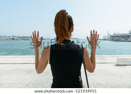 Back view of young woman outdoors at Port of Malaga Spain with arms raised against glass