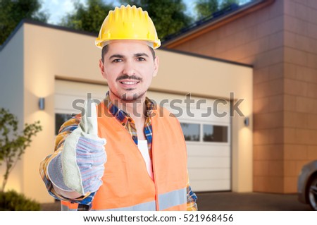 Portrait of handsome builder showing like or thumb up sign while standing outdoors with advertising area