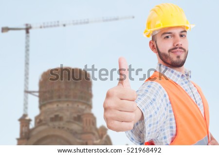 Handsome engineer showing thumb up in closeup with renovated building behind him and copyspace