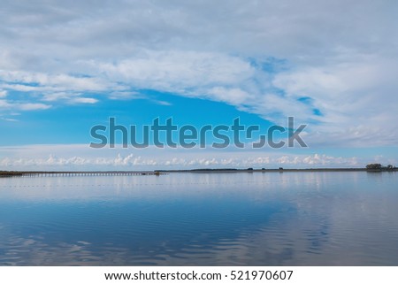 Blue sky reflected in a calm lake. White clouds reflected in a lake. Clouds hang low over the lake. Clear blue sky