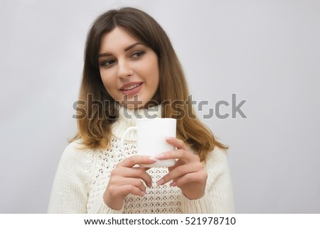 Portrait of young brunette woman in sweater drinking coffee or tea on light grey background