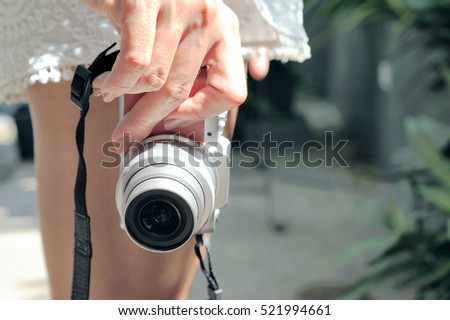 Woman wearing white short holding camera in her hand in the garden