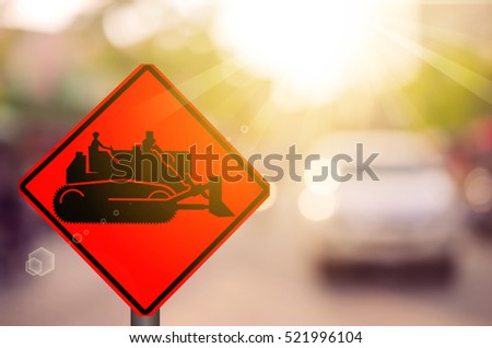 Construction tractor warning sign on blur traffic road with colorful bokeh light abstract background. Copy space of transportation and travel concept. Retro tone filter color style.