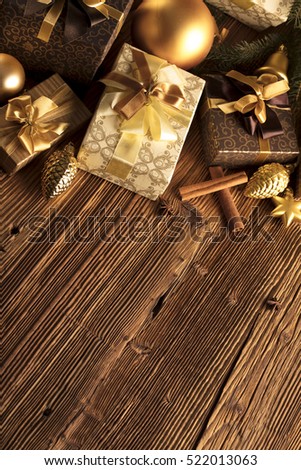 Christmas theme, christmas decoration. presents in boxes on a wooden table with golden baubles, clove, cardamon, star anise, cinnamon. Golden and brownish aesthetics. Place for typography and logo.
