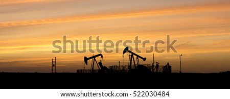 Silhouette of crude oil pump in oilfield at sunset - wide crop - black and white