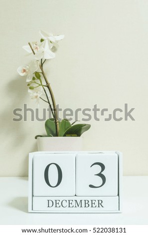 Closeup white wooden calendar with black 3 december word with white orchid flower on white wood desk and cream color wallpaper in room textured background , selective focus at the calendar