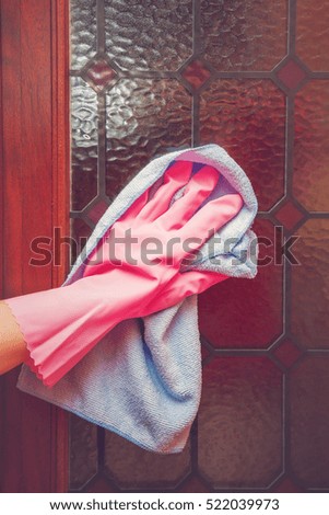 Hand in pink protective glove with rag cleaning dirty door with stained glass. Early spring cleaning or regular clean up. Maid cleans house. 