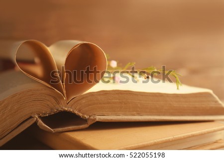 Old open book with heart made of pages on blurred background