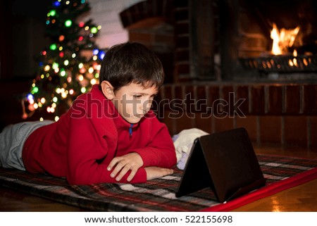 Boy watching tablet beside Christmas tree and fireplace