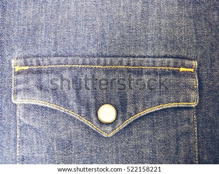 A close-up picture of a blue jean T-shirt front pocket with pearl-white button