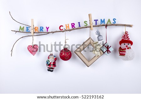 Christmas wooden thin branch with hanging toys, gifts and "Merry Christmas" greeting text writen with small colorful letters on white background